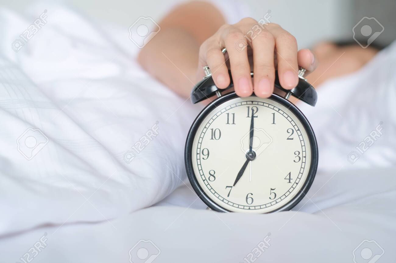 Woman lying in bed turning off an alarm clock in the morning at 5am. Hand  turns off the alarm clock waking up at morning, girl turns off the alarm  clock waking up, image size:1300x866