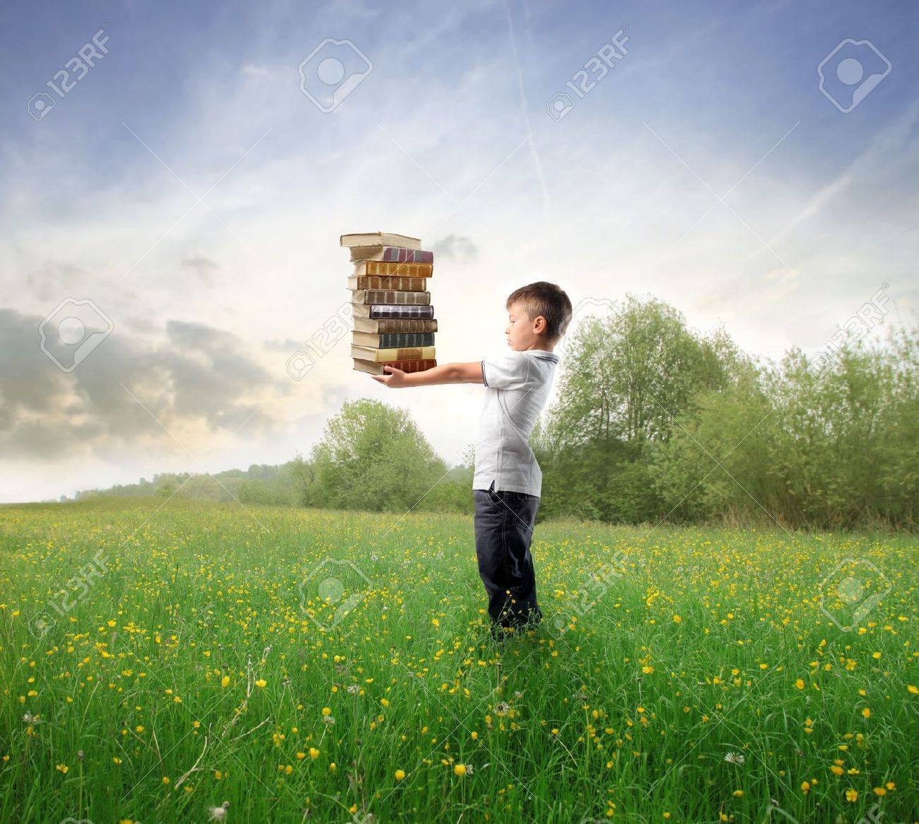 Child standing on a green meadowand holding some books - 8054408 Child standing on a green meadowand holding some books - 8054408