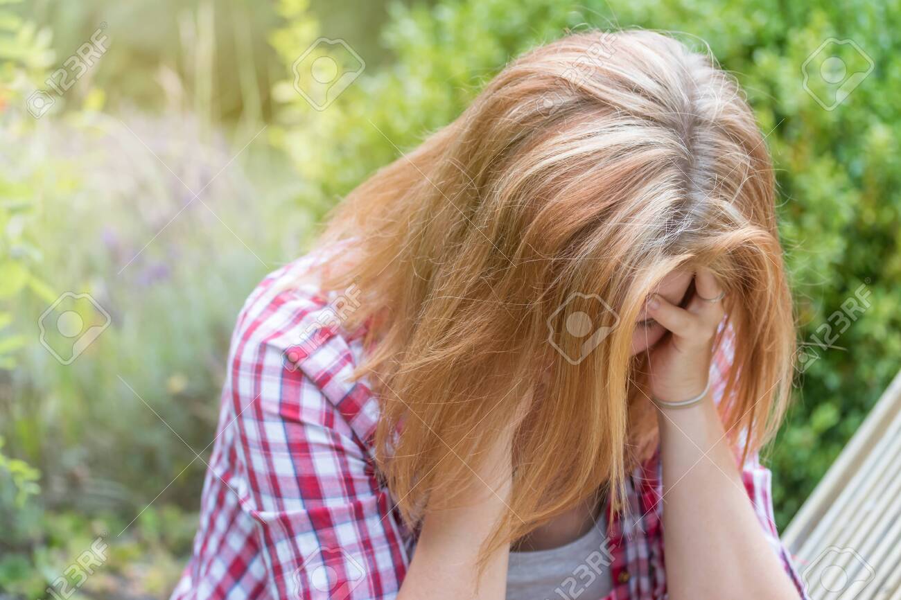 Attractive long haired young woman holding her hands over her head and looking down. She is depressed. - 129545423 Attractive long haired young woman holding her hands over her head and looking down. She is depressed. - 129545423