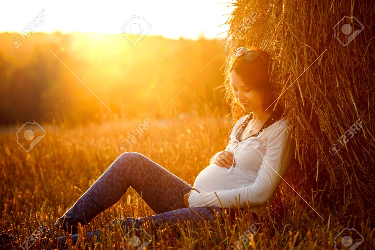 Young Pregnant Woman Sitting by the Haystack at Sunset and Embracing her Belly. 7 Month Pregnancy. Maternity Concept. Toned Photo. - 35965630 Young Pregnant Woman Sitting by the Haystack at Sunset and Embracing her Belly. 7 Month Pregnancy. Maternity Concept. Toned Photo. - 35965630