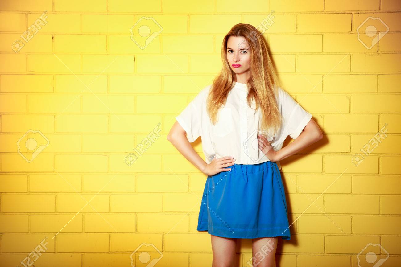 Portrait of Trendy Hipster Girl Making Duck Face with Hands on Hips. Yellow Brick Wall Background with Copy Space. Urban Fashion Concept. - 38918966 Portrait of Trendy Hipster Girl Making Duck Face with Hands on Hips. Yellow Brick Wall Background with Copy Space. Urban Fashion Concept. - 38918966