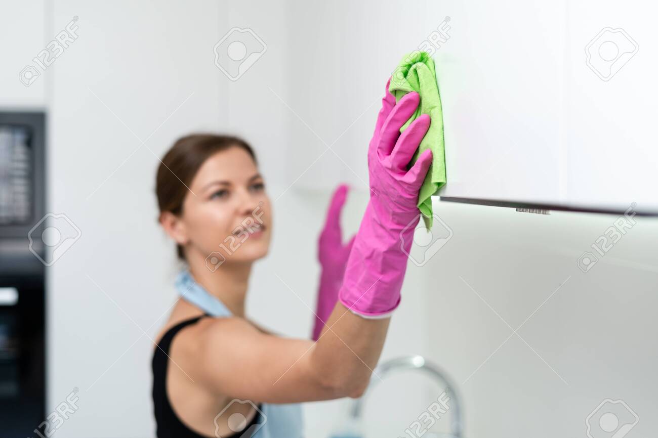 Selective focus of young adult housewife in apron and rubber gloves using wipe cloth and cleaning contemporary white kitchen cabinet at home - 129006569 Selective focus of young adult housewife in apron and rubber gloves using wipe cloth and cleaning contemporary white kitchen cabinet at home - 129006569