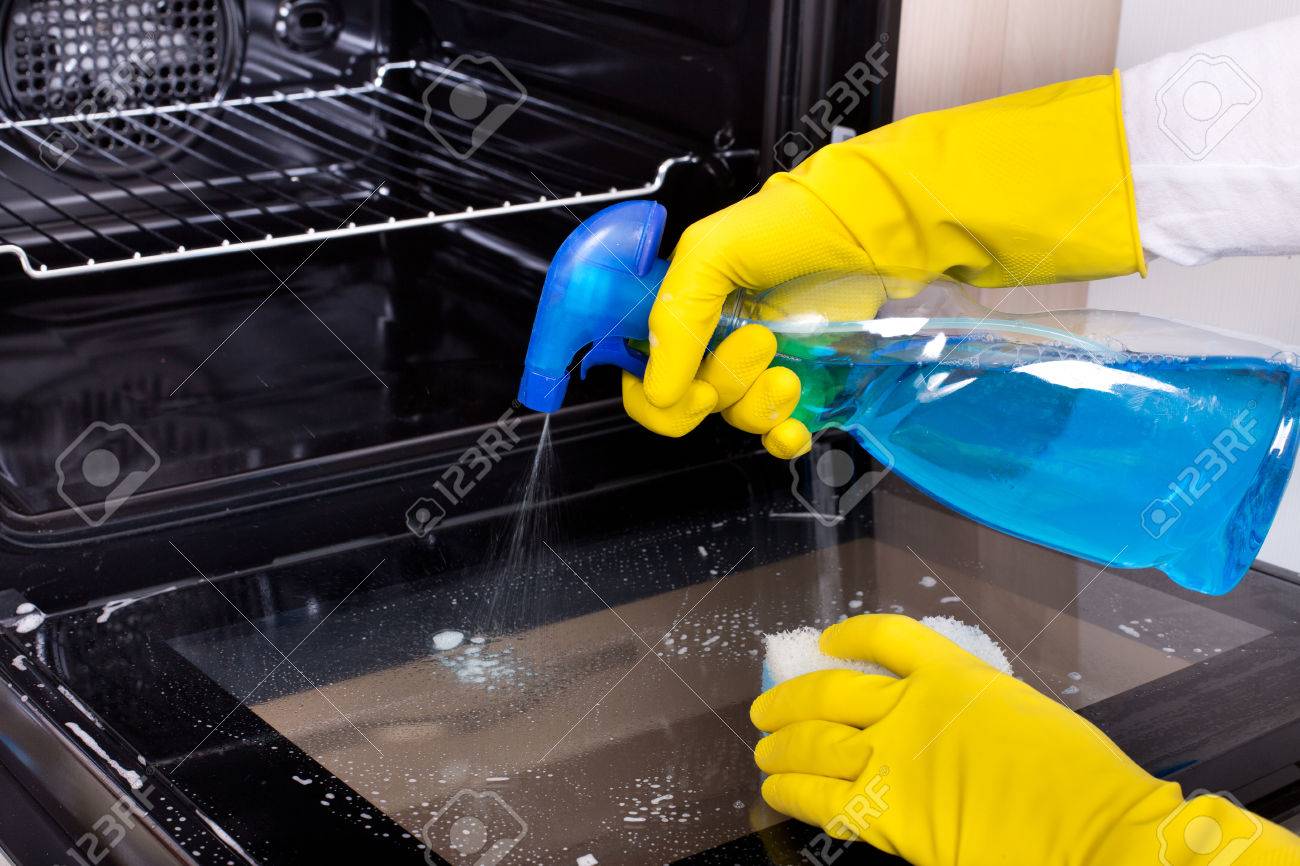 Close up of female hand with yellow protective gloves spraying detergent from bottle on the oven door - 50442976 Close up of female hand with yellow protective gloves spraying detergent from bottle on the oven door - 50442976
