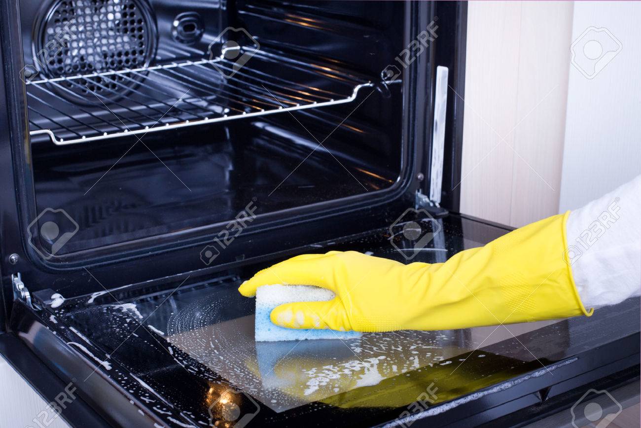 Close up of female hand with yellow protective gloves cleaning oven door - 50443285 Close up of female hand with yellow protective gloves cleaning oven door - 50443285
