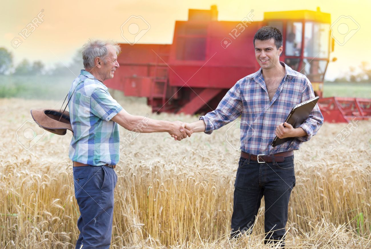 Two farmers shaking hands on wheat field while combine harvesting behind - 59605842 Two farmers shaking hands on wheat field while combine harvesting behind - 59605842