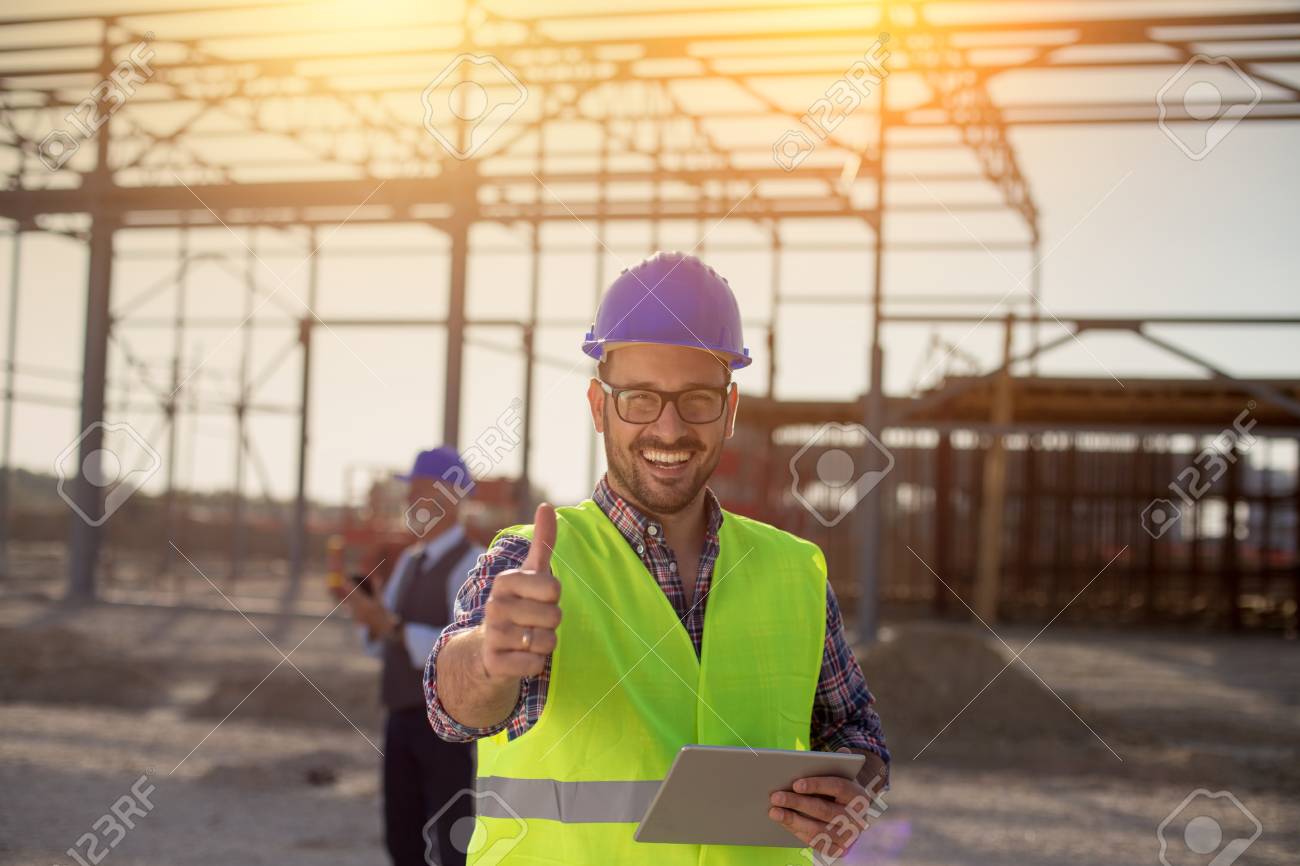 Portrait of satisfied engineer holding tablet and showing thumb up on building site - 115960818 Portrait of satisfied engineer holding tablet and showing thumb up on building site - 115960818