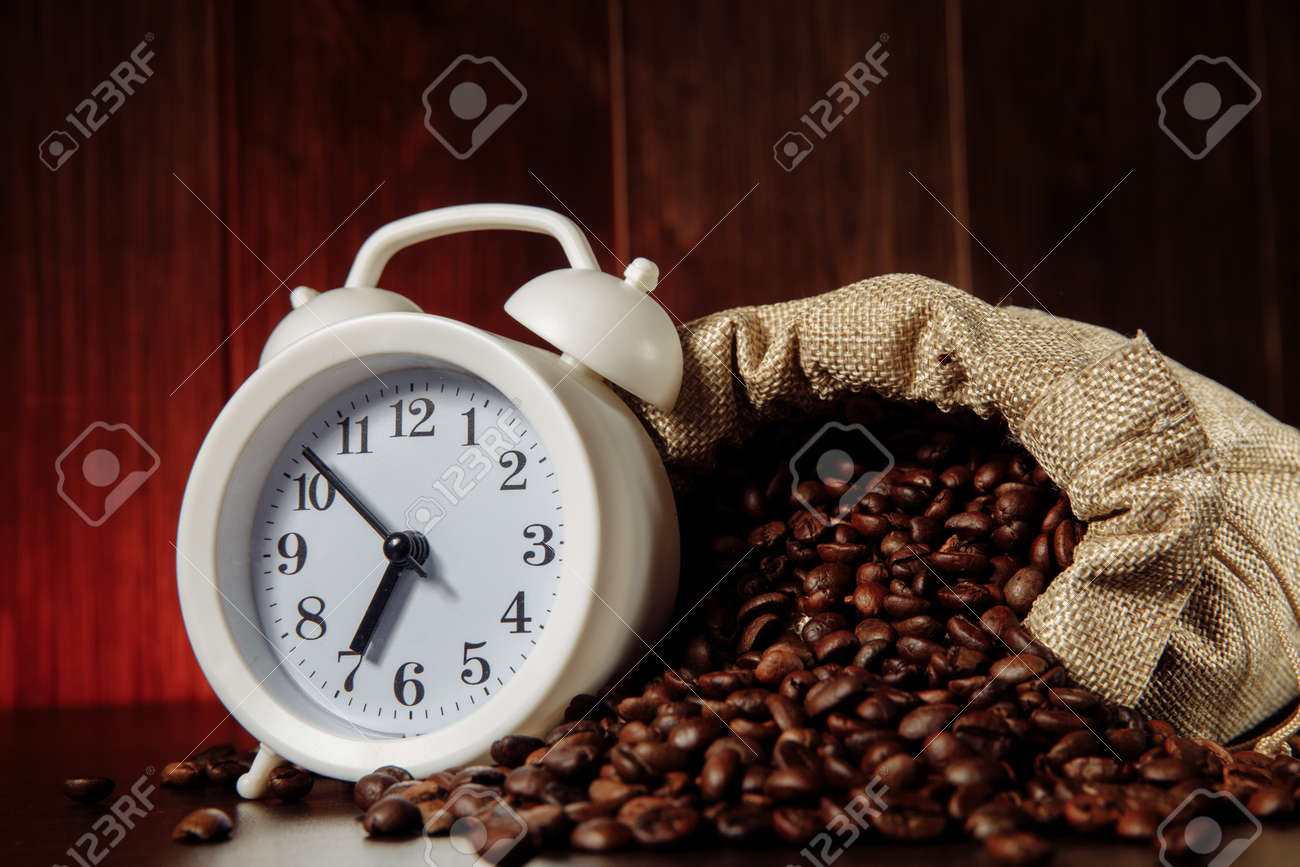 A white alarm clock and coffee beans in a sack bag close-up - 169820856 A white alarm clock and coffee beans in a sack bag close-up - 169820856