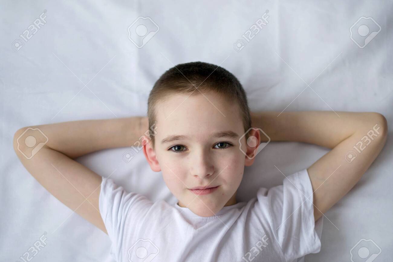 Top View Of A Boy Who Is Lying In Bed And Folded His Arms Behind His Head The Child Lies On His Back On A White Background Stock Photo Picture And Royalty