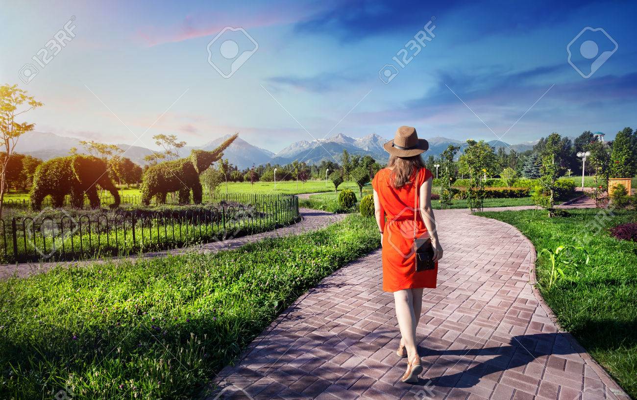 Woman in orange dress walking down the road in Topiary Garden with elephants from plants - 60232468 Woman in orange dress walking down the road in Topiary Garden with elephants from plants - 60232468