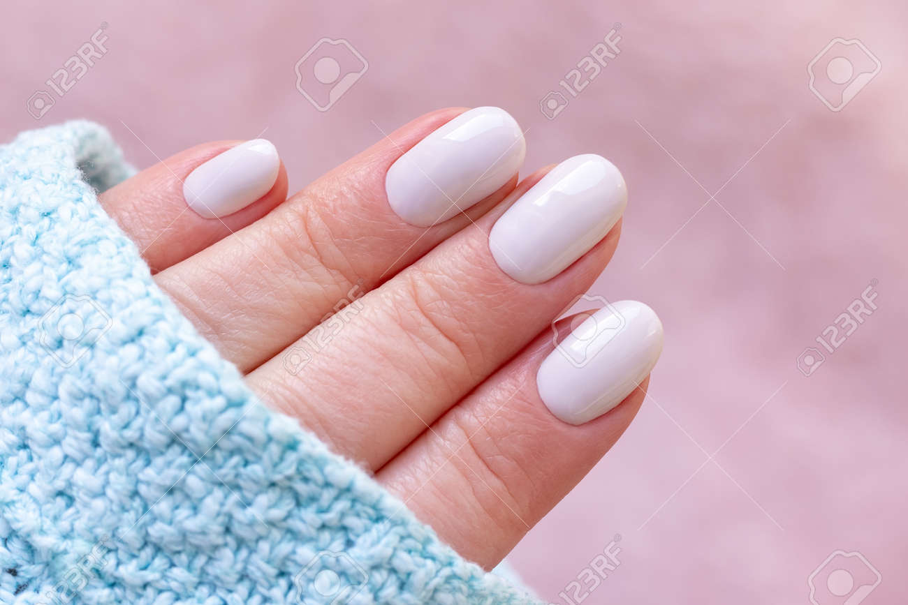 Female hand in blue knitted sweater with beautiful manicure - white ivory nails on blurred pale pink background - 169497553 Female hand in blue knitted sweater with beautiful manicure - white ivory nails on blurred pale pink background - 169497553