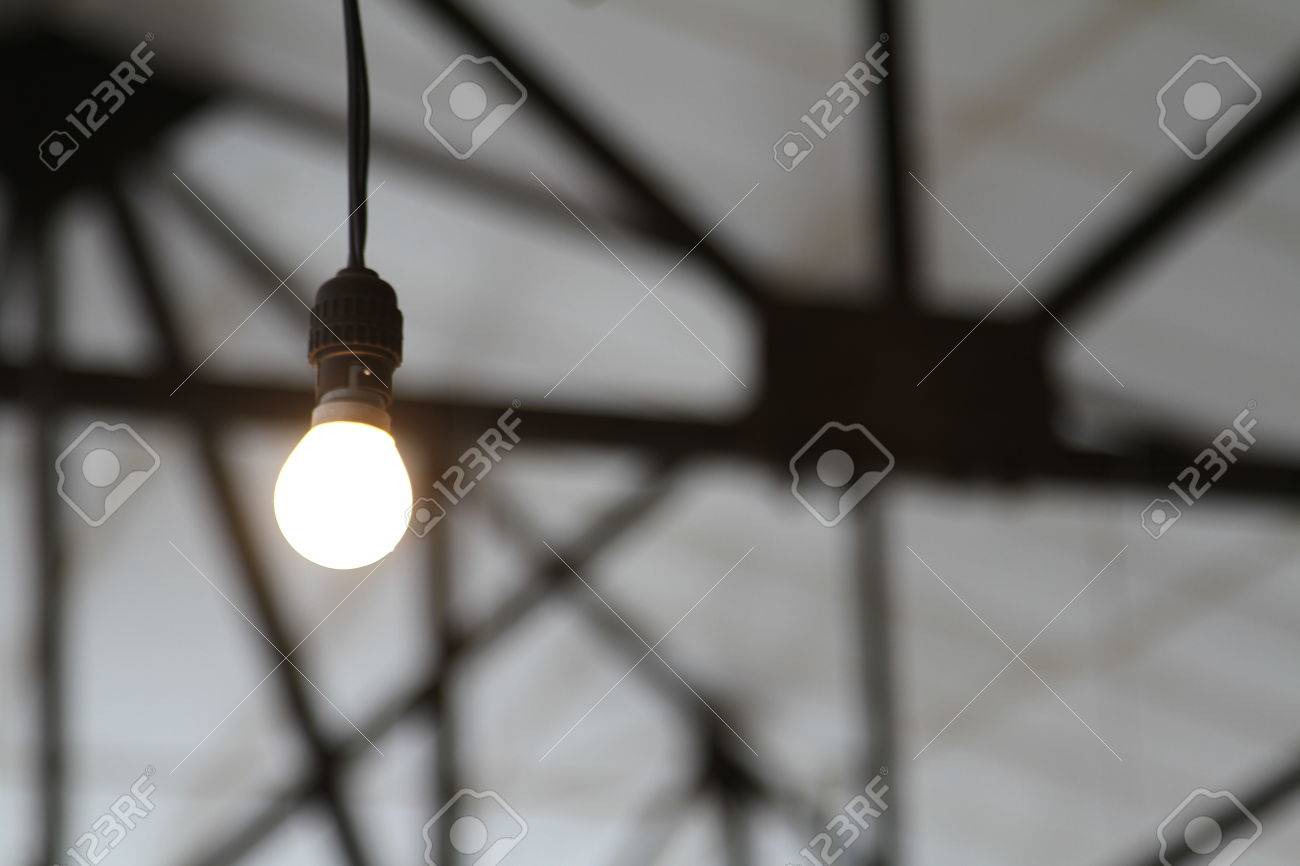 bare industrial light bulb with roofing girders low key stock photo