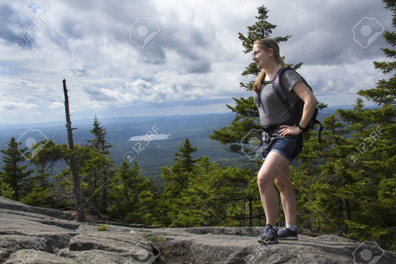 Mujer Adulta Joven En Pantalones Cortos, De Excursión Con Una Mochila Sobre Un Sendero Rocoso, Que Se Coloca En Cumbre Del Monte Kearsarge, New Hampshire, A La Izquierda. Fotos, Retratos, Imágenes