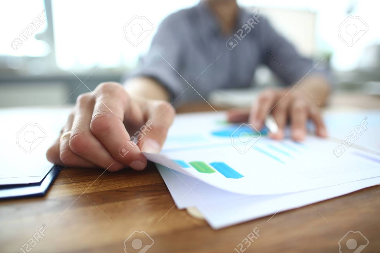 Close up of young businessman holding paper with financial information, editing documents, explaining marketing strategy or planning company economic growth at brainstorming meeting at office. - 134821466 Close up of young businessman holding paper with financial information, editing documents, explaining marketing strategy or planning company economic growth at brainstorming meeting at office. - 134821466
