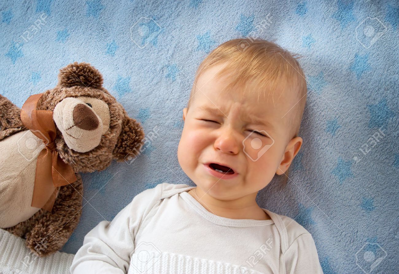 One year old baby lying in bed holding a plush teddy bear - 46496815 One year old baby lying in bed holding a plush teddy bear - 46496815