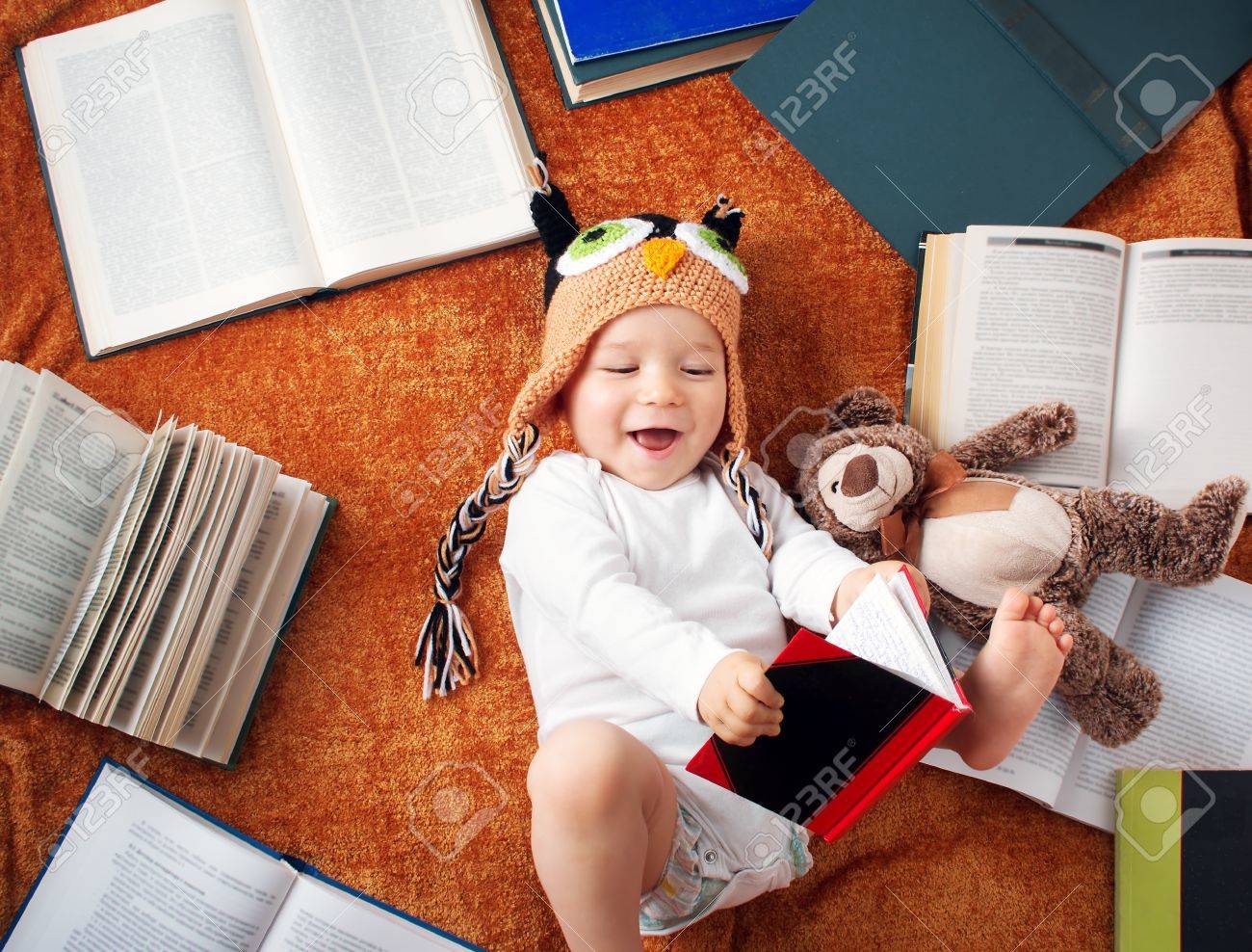 one year old baby in owl hat reading books with teddy bear stock