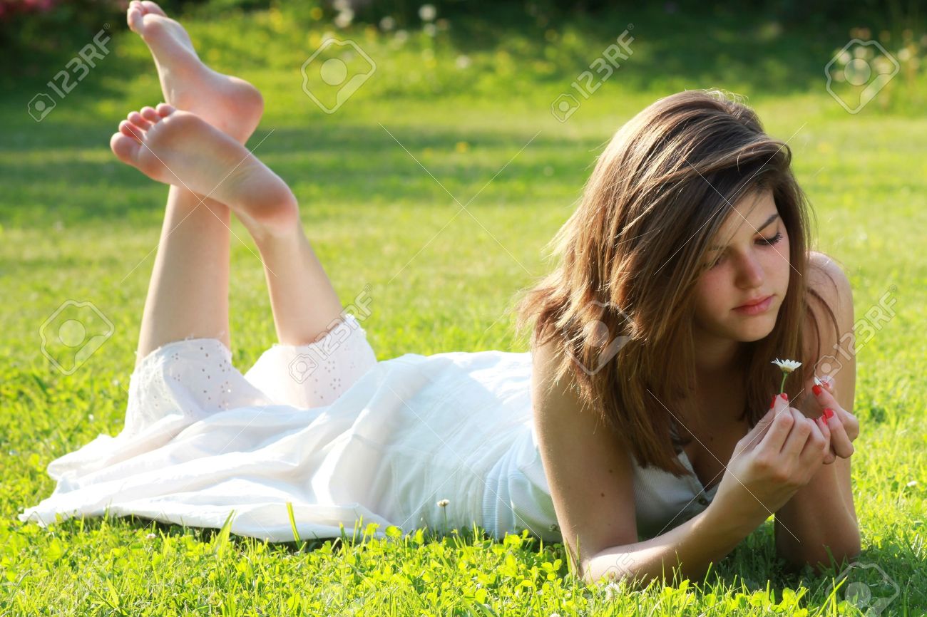 pretty young girl is tearing petals from a daisy lying on grass