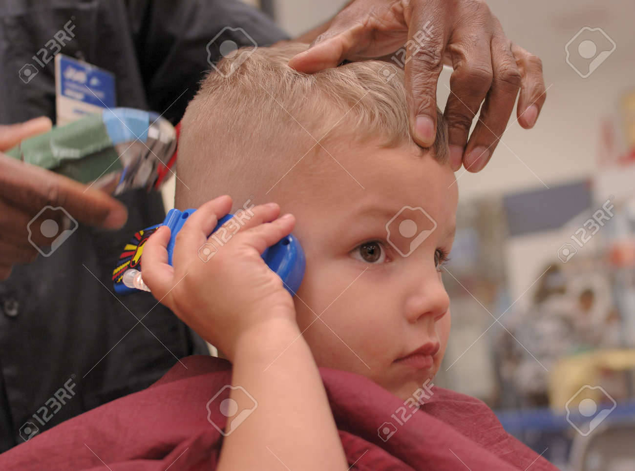 A 3 Year Old Boy Talks On A Toy Cell Phone While Getting A Haircut