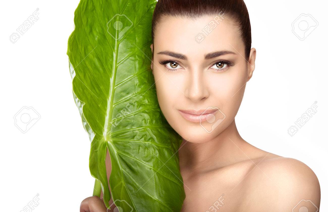 Beauty and skincare portrait. Beautiful spa girl with the large fresh green leaf of a tropical plant against her cheek as she looks at the camera with a gentle smile in a spa and wellness concept - 55314682 Beauty and skincare portrait. Beautiful spa girl with the large fresh green leaf of a tropical plant against her cheek as she looks at the camera with a gentle smile in a spa and wellness concept - 55314682