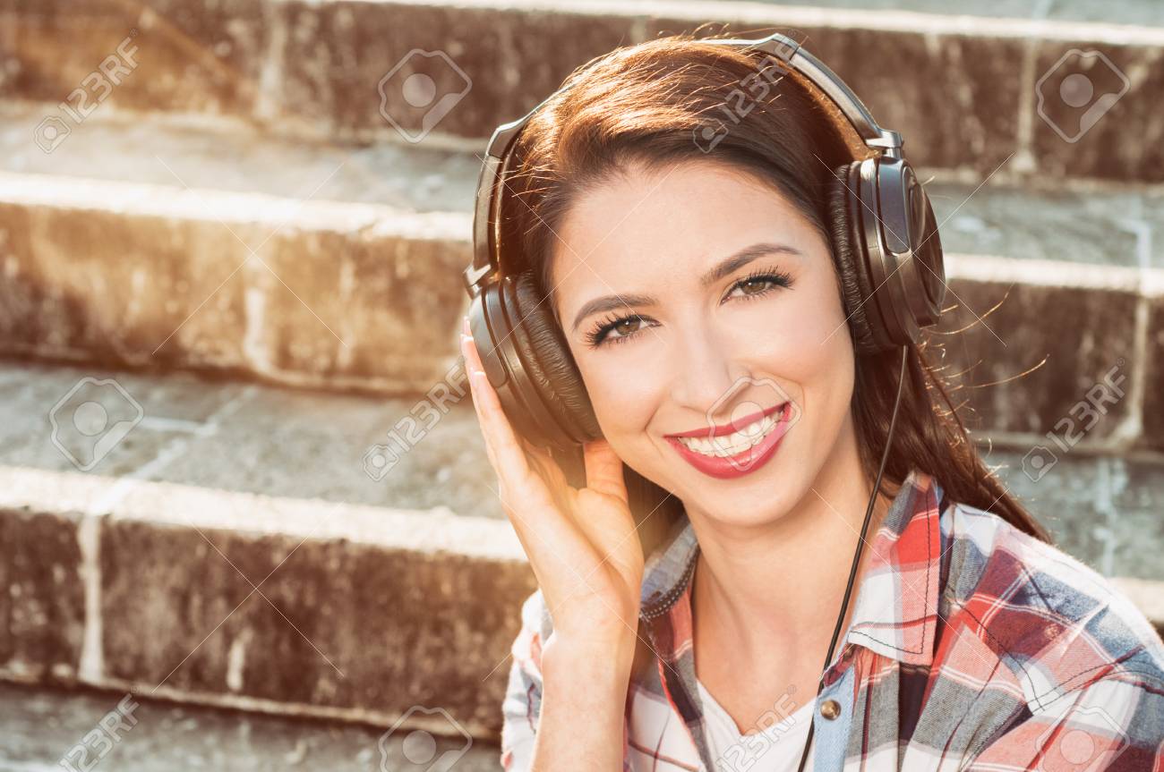 屈託のない笑顔と外の公園でヘッドホンで音楽を聞いて美しい女性コンセプト の写真素材 画像素材 Image