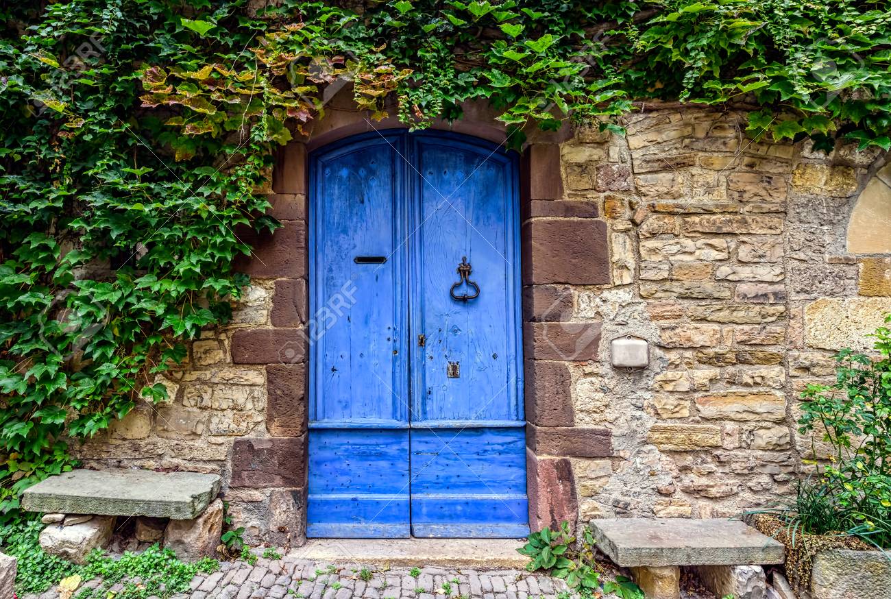 A blue and worn door with green ivy above on the stone walls of a small town in French countryside - 92543608 A blue and worn door with green ivy above on the stone walls of a small town in French countryside - 92543608
