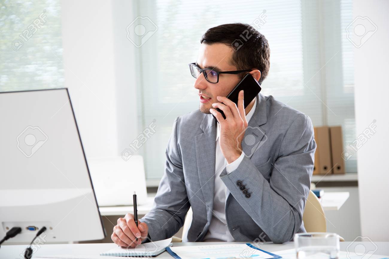 Young handsome businessmantalking on the phone in an office - 116694936 Young handsome businessmantalking on the phone in an office - 116694936