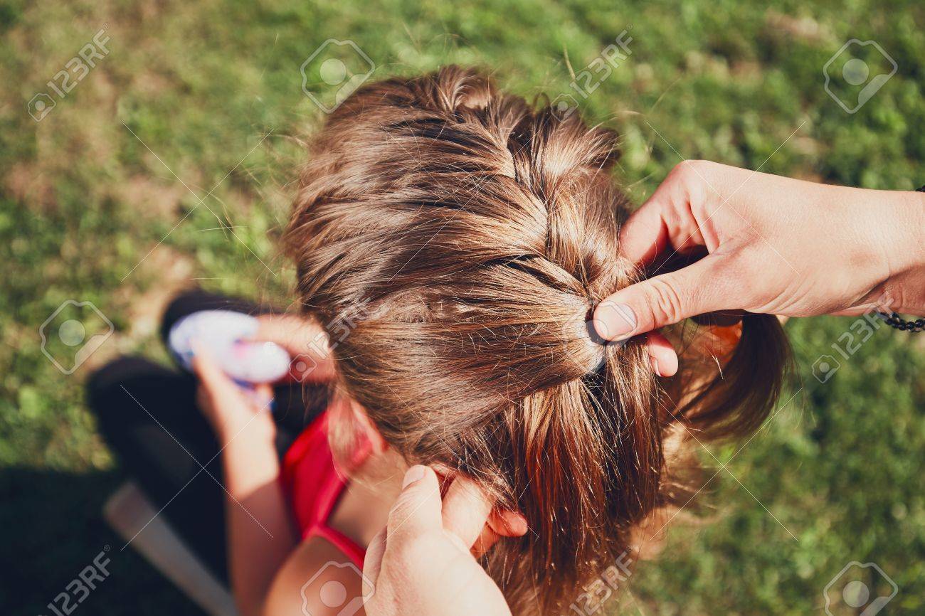 Young Woman Making Hair Braids Of The Little Girl On The Garden