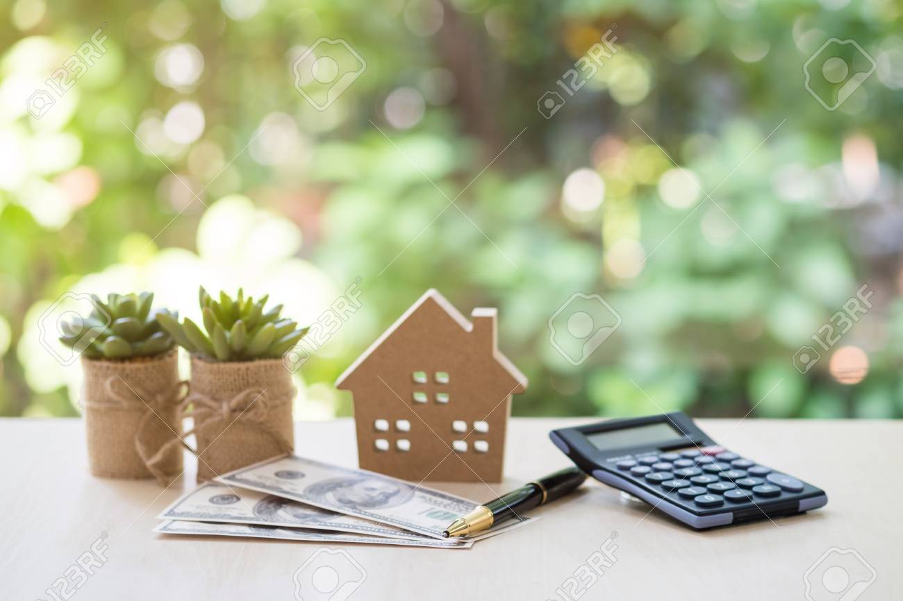 Home Loan, mortgage and real estate concept, House model with pile of dollar bills, calculator, pen and plant pots on table with garden background for business, finance, banking, and saving money. - 100807989 Home Loan, mortgage and real estate concept, House model with pile of dollar bills, calculator, pen and plant pots on table with garden background for business, finance, banking, and saving money. - 100807989
