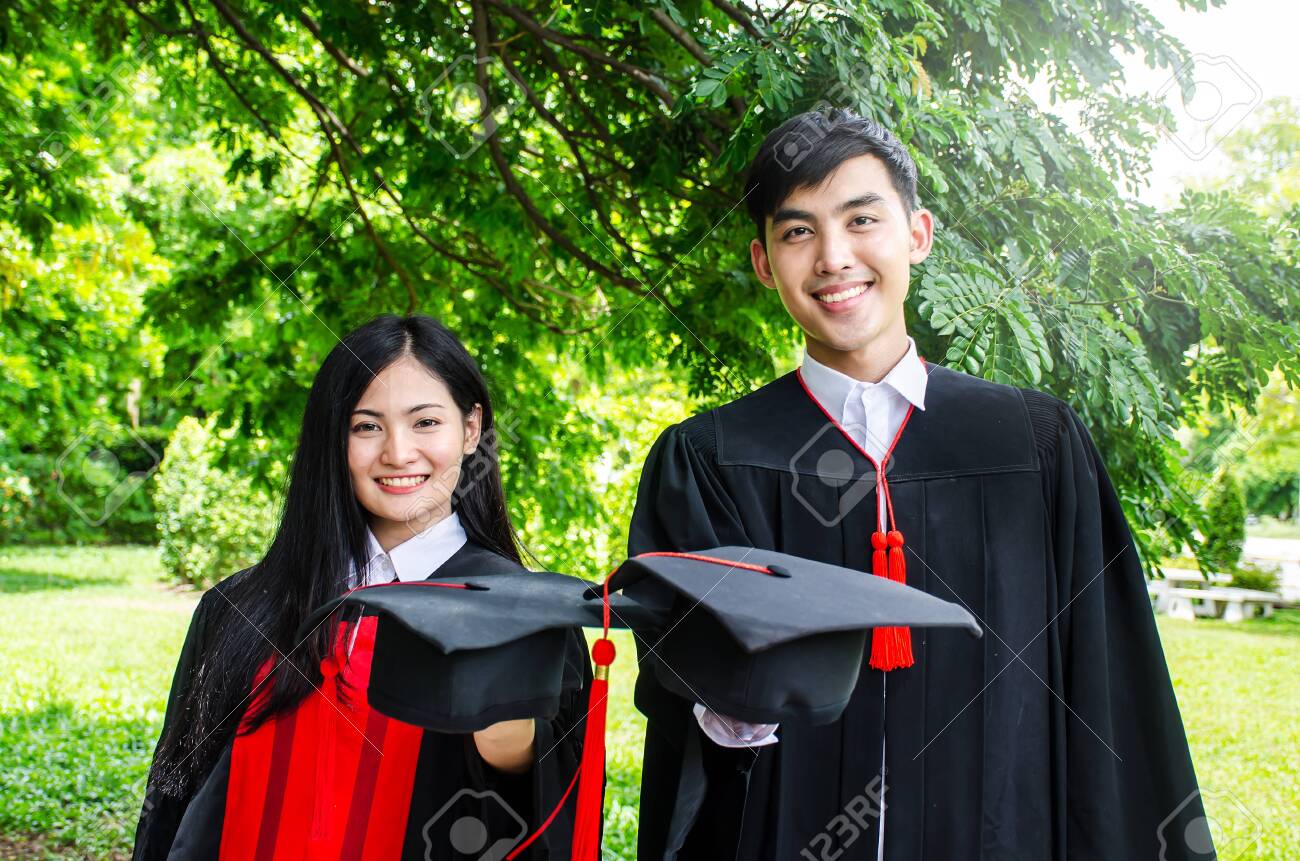 Una Pareja De Hombres Y Mujeres Vestidos Con Un Vestido Negro De Graduación O Graduados Con Felicitaciones Con Sombreros De Graduación Está De Pie, Sonriendo Y Sosteniendo Un Sombrero Con El Fondo Una Pareja De Hombres Y Mujeres Vestidos Con Un Vestido Negro De Graduación O Graduados Con Felicitaciones Con Sombreros De Graduación Está De Pie, Sonriendo Y Sosteniendo Un Sombrero Con El Fondo