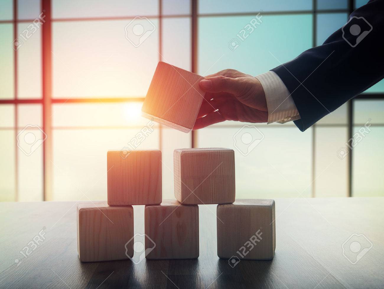 The concept of planning in business. Wooden cubes on a desk in the office. The concept of leadership. Hand men in business suit holding the cubes. - 52484027 The concept of planning in business. Wooden cubes on a desk in the office. The concept of leadership. Hand men in business suit holding the cubes. - 52484027