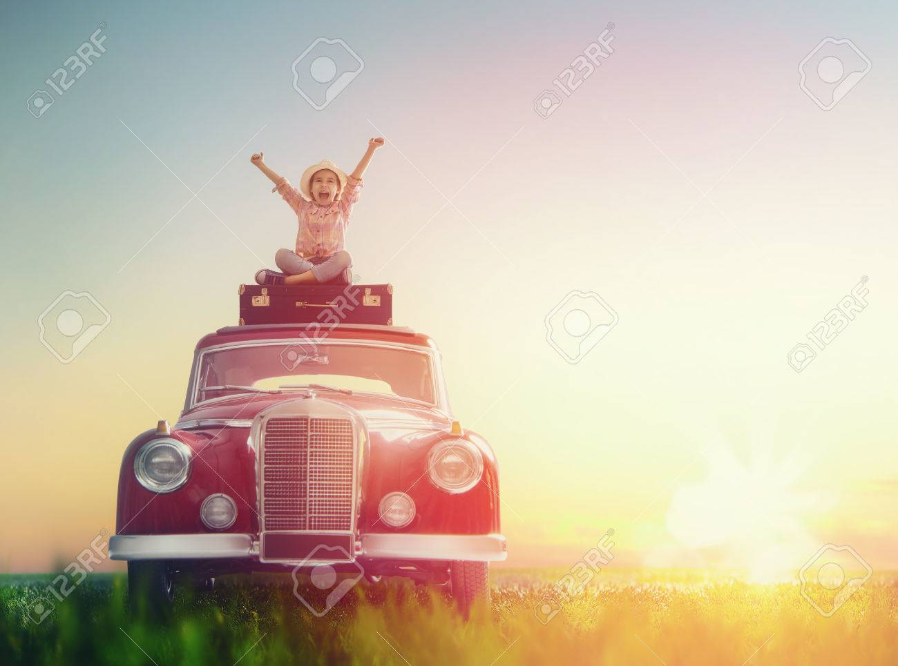 Toward adventure! Girl relaxing and enjoying road trip. Happy child girl sitting on roof of vintage car. - 55594998 Toward adventure! Girl relaxing and enjoying road trip. Happy child girl sitting on roof of vintage car. - 55594998