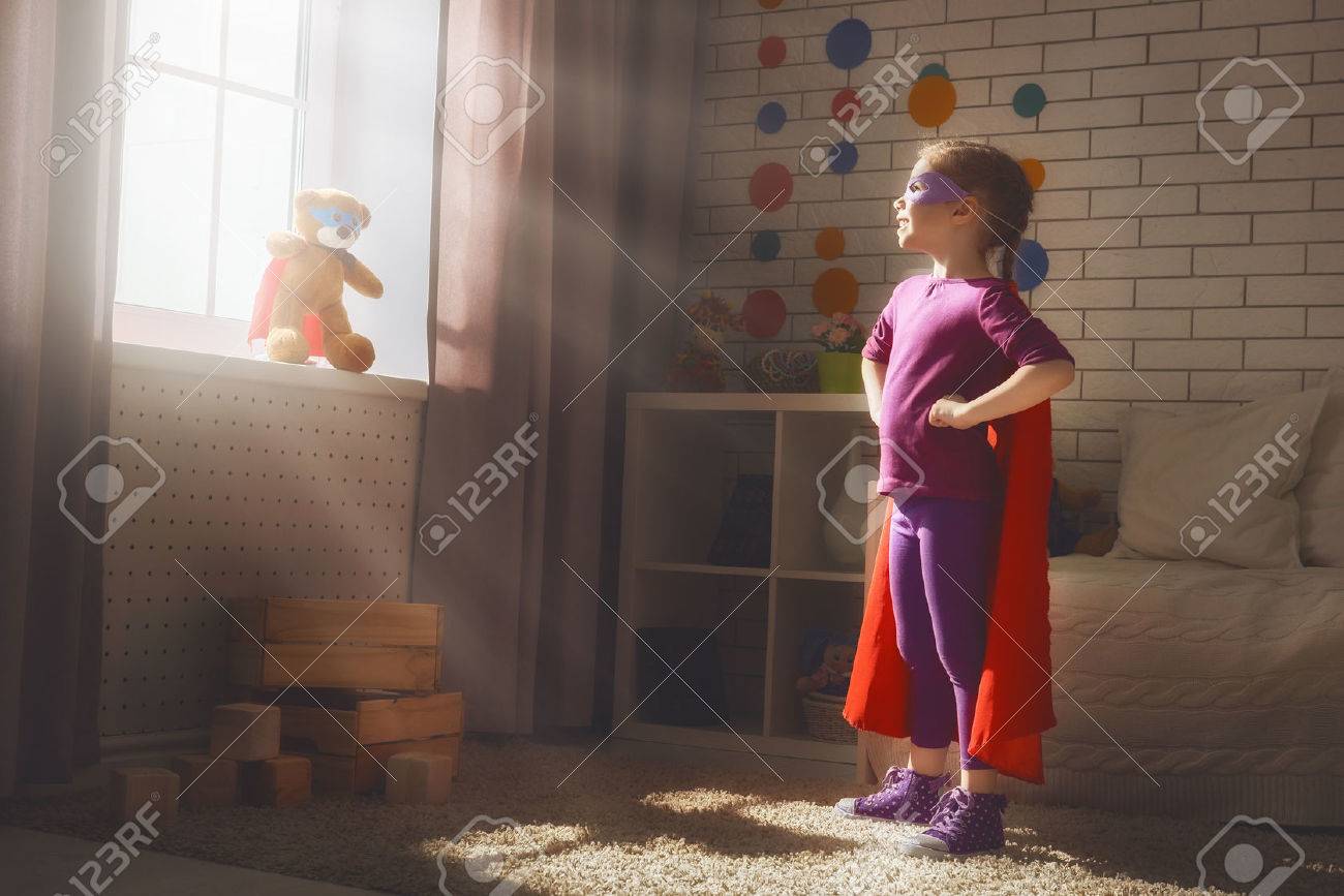 Little child girl plays superhero. Child plays with her friend a Teddy bear. Girl power concept. - 56618646 Little child girl plays superhero. Child plays with her friend a Teddy bear. Girl power concept. - 56618646