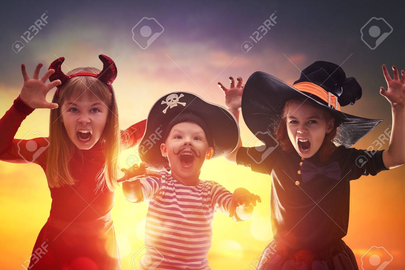 Happy brother and two sisters on Halloween. Funny kids in carnival costumes outdoors. Cheerful children on sunset background. - 62765541 Happy brother and two sisters on Halloween. Funny kids in carnival costumes outdoors. Cheerful children on sunset background. - 62765541