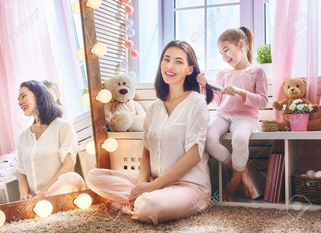 幸せな愛情のある家族 かわいい女の子は 子供部屋の鏡の近くに座っている彼女の母の髪をとかすです の写真素材 画像素材 Image
