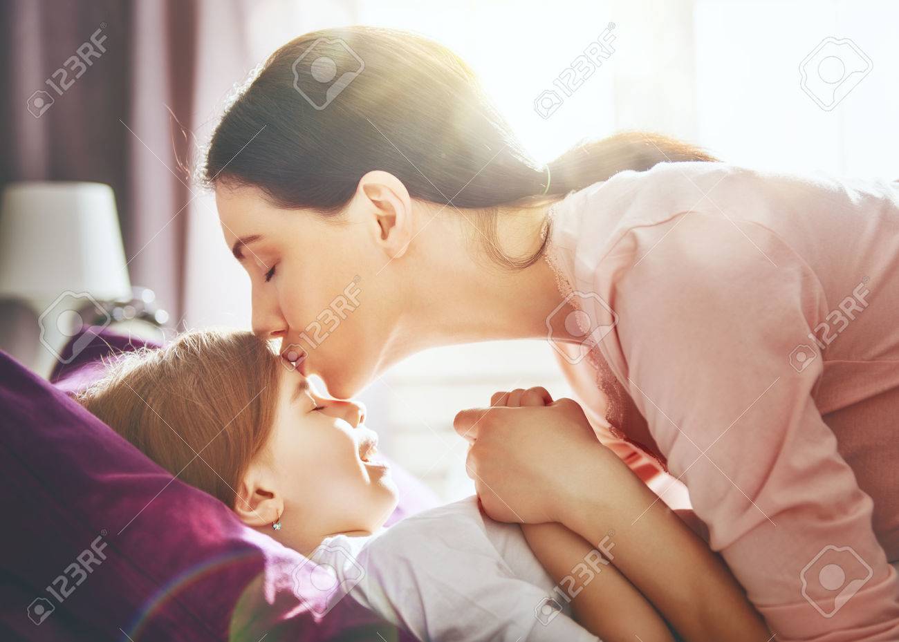 A Nice Girl And Her Mother Enjoy Sunny Morning Good Time At Home Child Sleeps The Mom Wakes The Kid With A Kiss On The Bed In The Bedroom Stock Photo Picture