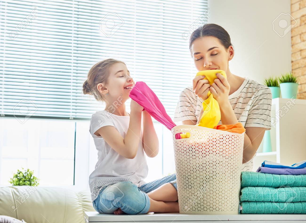 Beautiful young woman and child girl little helper are smelling clean clothes and smiling while doing laundry at home. - 77784663 Beautiful young woman and child girl little helper are smelling clean clothes and smiling while doing laundry at home. - 77784663