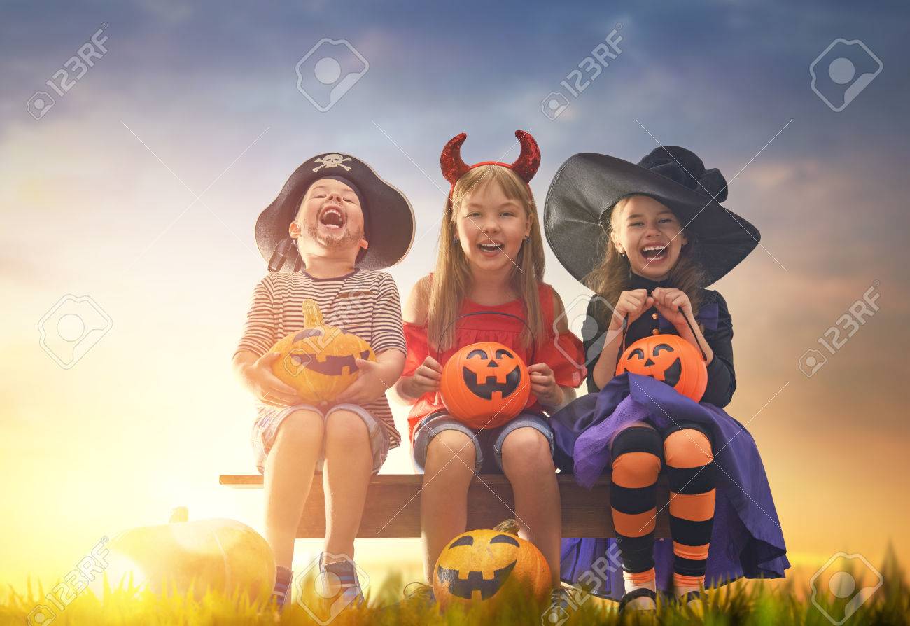 Happy brother and two sisters at Halloween. Funny kids in carnival costumes outdoors. Cheerful children and pumpkins on sunset background. - 85131483 Happy brother and two sisters at Halloween. Funny kids in carnival costumes outdoors. Cheerful children and pumpkins on sunset background. - 85131483