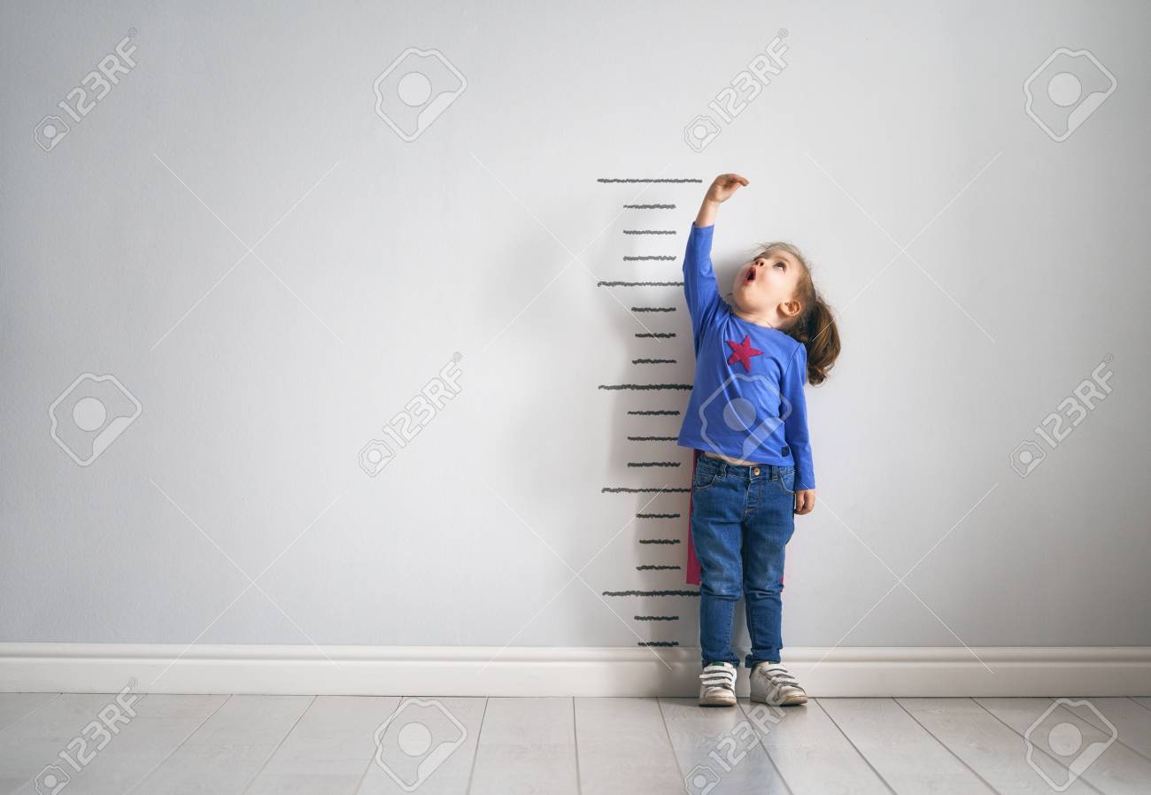 Little child is playing superhero. Kid is measuring the growth on the background of wall. Girl power concept. - 99197356 Little child is playing superhero. Kid is measuring the growth on the background of wall. Girl power concept. - 99197356