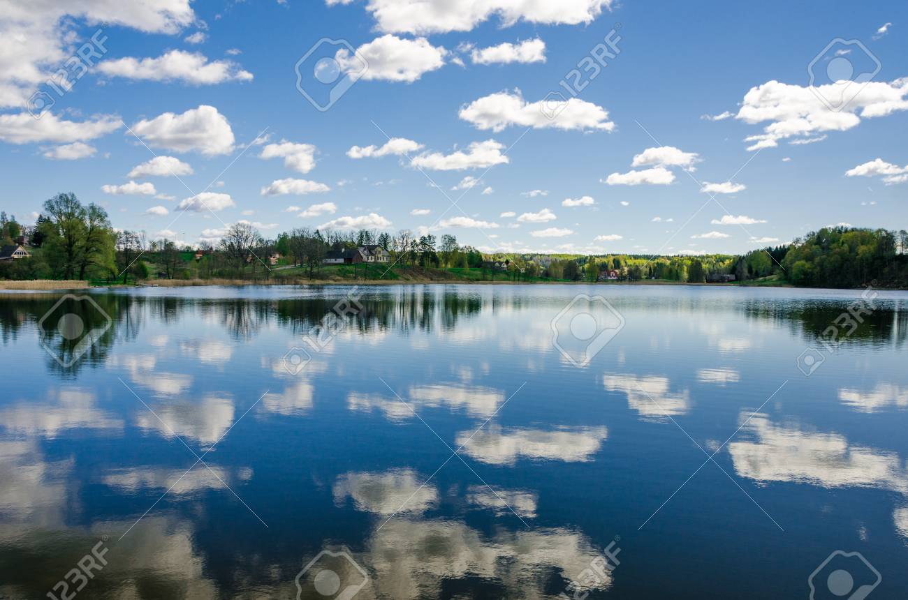 Cloudy blue sky reflects into the lake with trees on the horizon. - 77455849 Cloudy blue sky reflects into the lake with trees on the horizon. - 77455849
