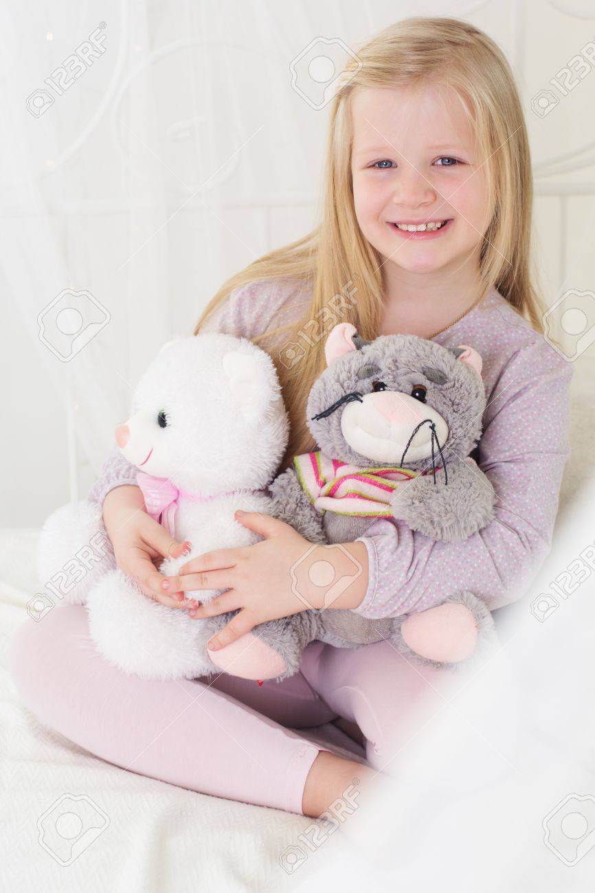 happy blonde child girl is holding her soft toys in the bed stock