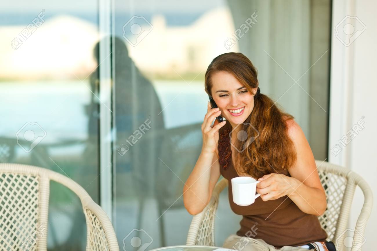 幸せな女の子の携帯電話を話すとテラスでコーヒーのカップを持っていること の写真素材 画像素材 Image