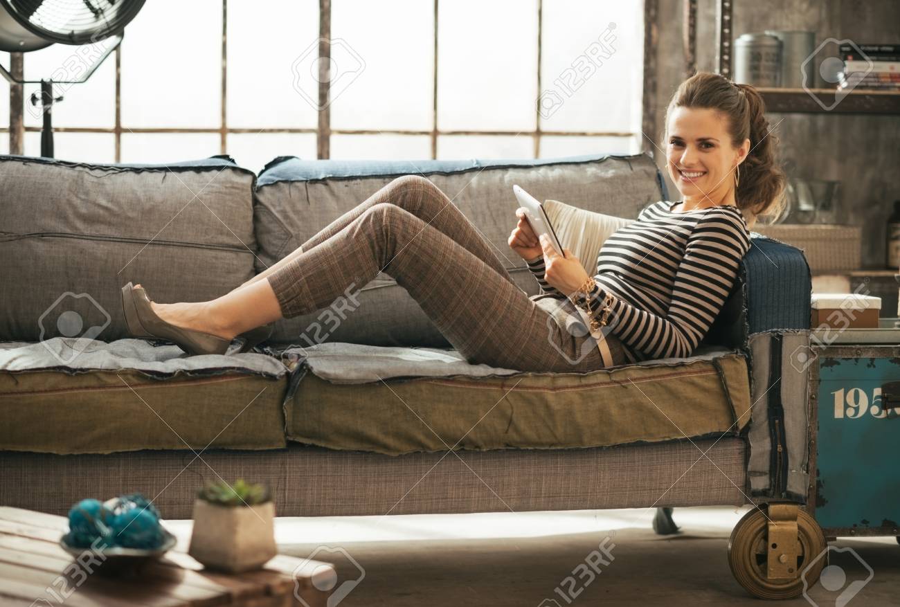 Smiling young woman laying on divan and using tablet pc in loft apartment - 40310543 Smiling young woman laying on divan and using tablet pc in loft apartment - 40310543