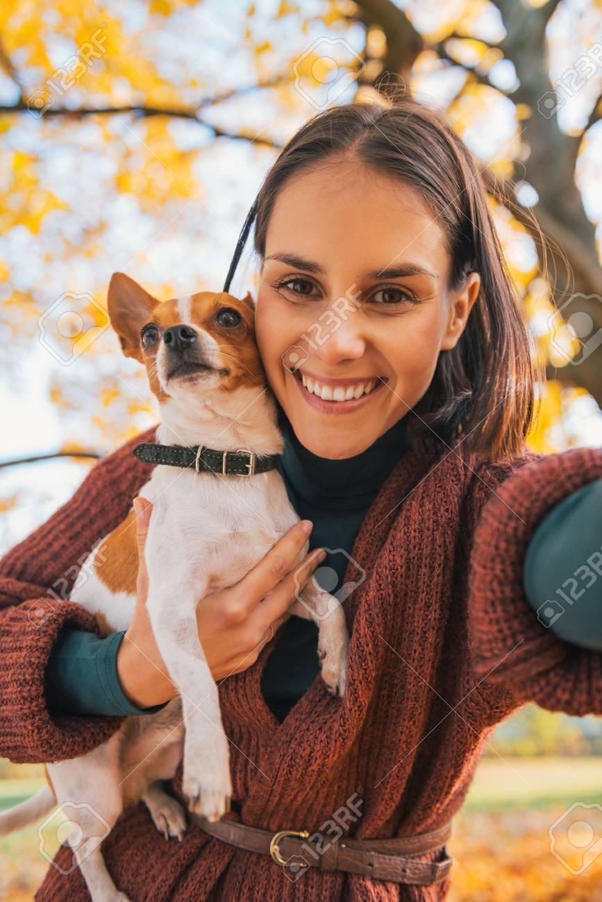 Portrait of smiling young woman with dog outdoors in autumn making selfie - 40310899 Portrait of smiling young woman with dog outdoors in autumn making selfie - 40310899