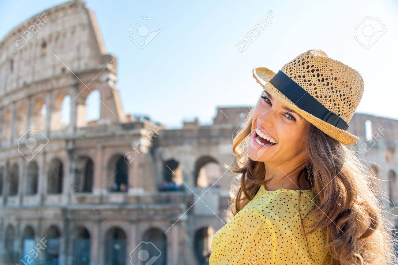 A woman is turning and looking over her shoulder while laughing, enjoying being a tourist in the beautiful city of Rome. In the background, the Colosseum. - 40568262 A woman is turning and looking over her shoulder while laughing, enjoying being a tourist in the beautiful city of Rome. In the background, the Colosseum. - 40568262