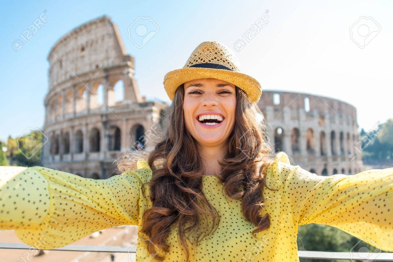 A happy, smiling woman tourist in the summer takes a selfie with the Colosseum in the distance. - 40568350 A happy, smiling woman tourist in the summer takes a selfie with the Colosseum in the distance. - 40568350