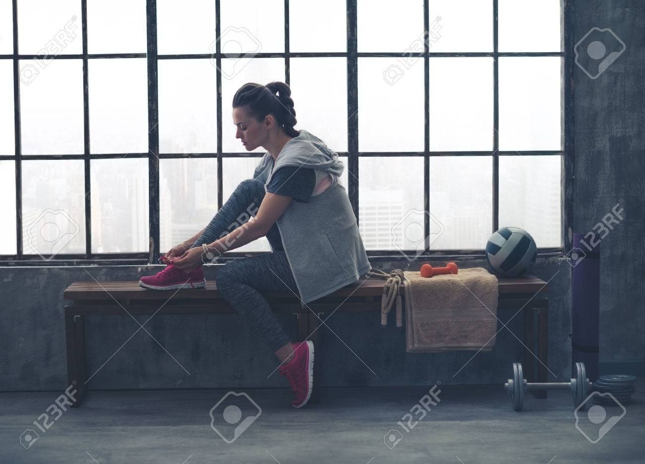 A quiet moment to tie her shoes. A fit, sporty young woman has one foot up on a bench, tying her shoelaces, as she gets ready to start her workout. - 43887546 A quiet moment to tie her shoes. A fit, sporty young woman has one foot up on a bench, tying her shoelaces, as she gets ready to start her workout. - 43887546
