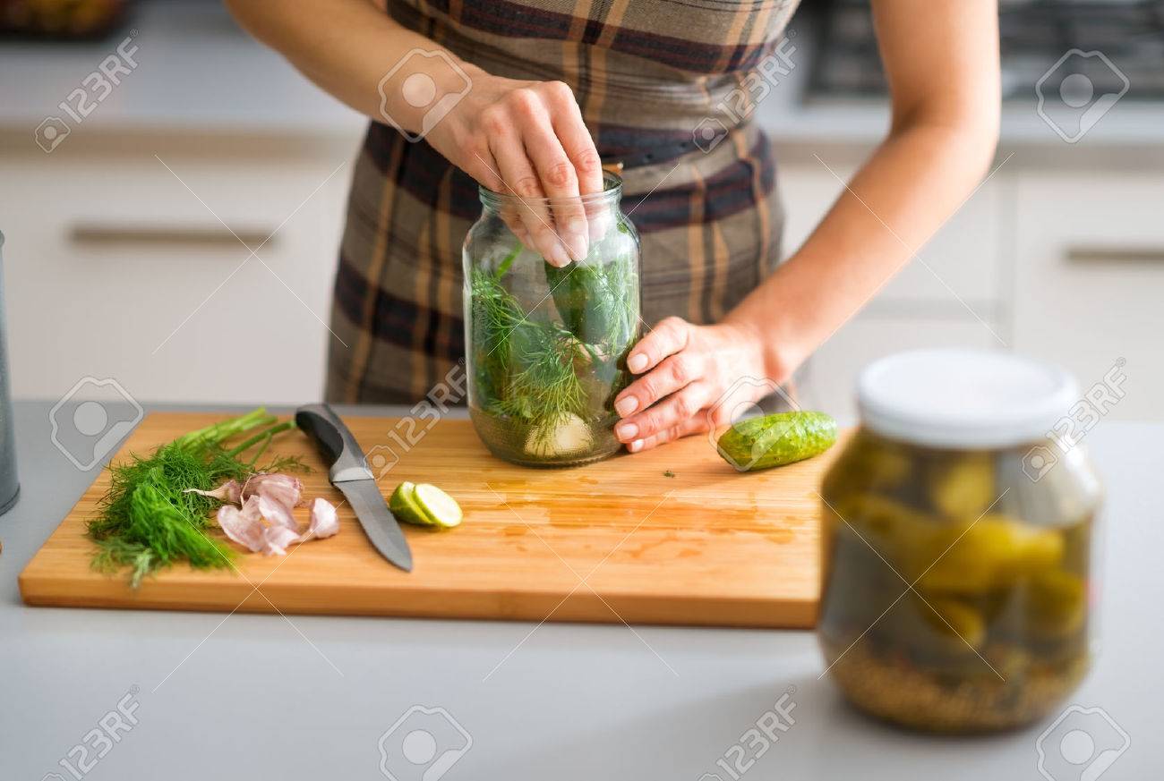 Step by step, the flavors come together. Here, a woman's hands are hard at work, stuffing cucumbers and dill into a pickling jar as she prepares home-made dill pickles. - 45218511 Step by step, the flavors come together. Here, a woman's hands are hard at work, stuffing cucumbers and dill into a pickling jar as she prepares home-made dill pickles. - 45218511