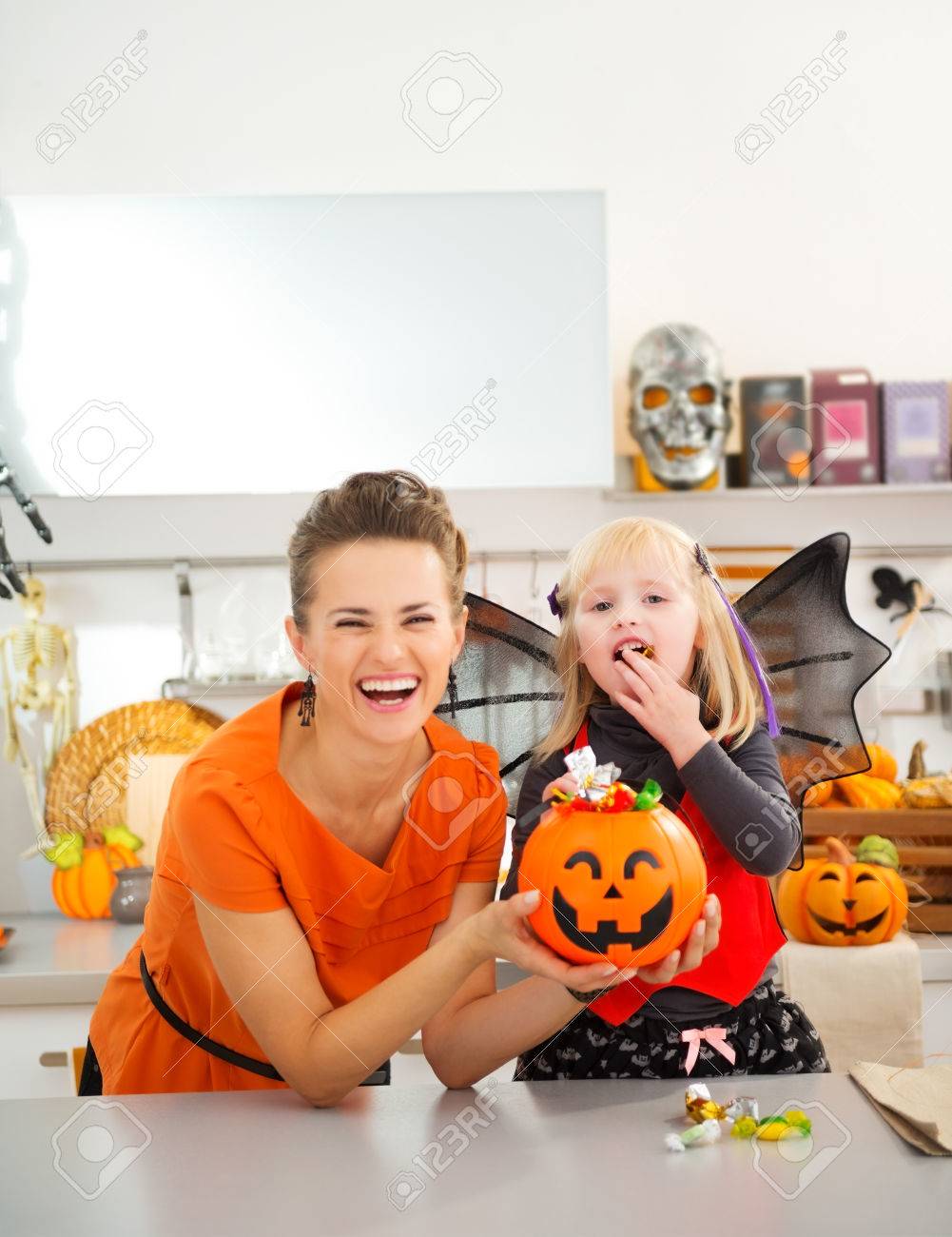 Happy young mother with daughter in bat costume eating colorfull halloween candy in decorated kitchen. Halloween Candy is so good. Traditional autumn holiday - 45391819 Happy young mother with daughter in bat costume eating colorfull halloween candy in decorated kitchen. Halloween Candy is so good. Traditional autumn holiday - 45391819