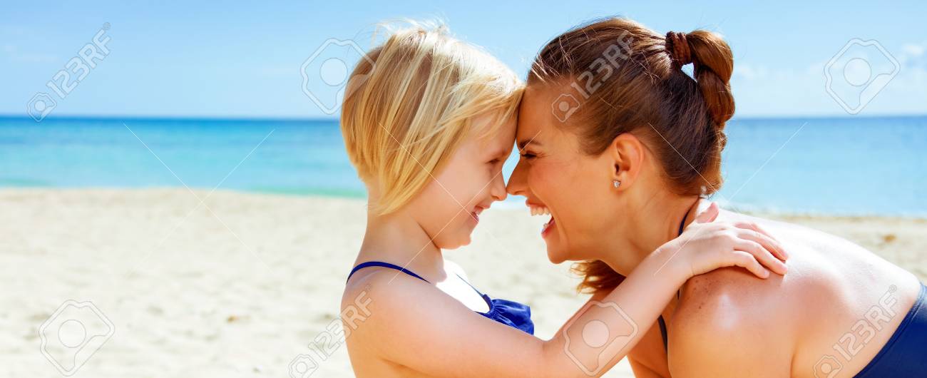 太陽は美しさにキスをした 抱きしめる海岸で水着で幸せな健康な母と子供 の写真素材 画像素材 Image