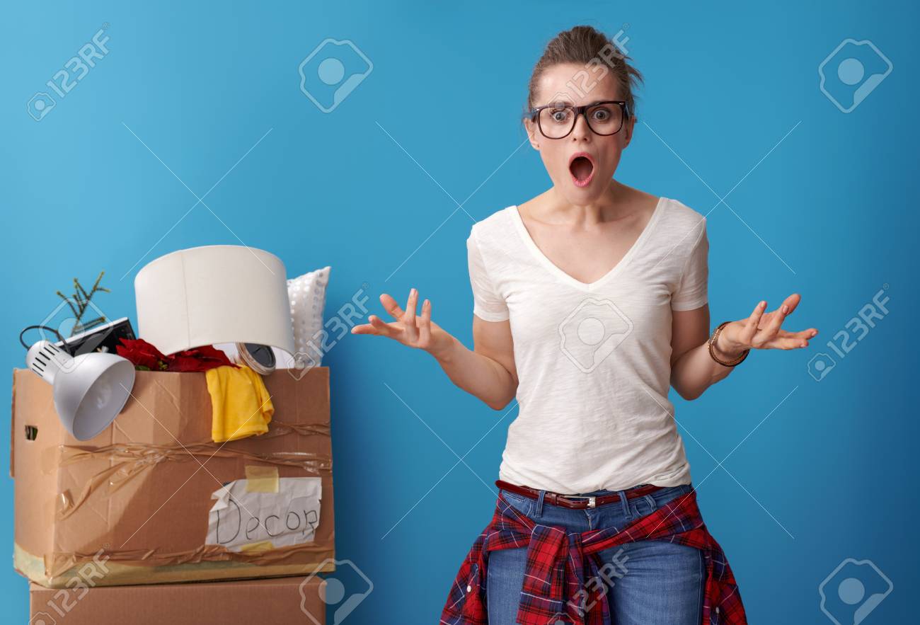 shocked modern woman in white shirt with an untidy cardboard box in the background isolated on blue - 103329613 shocked modern woman in white shirt with an untidy cardboard box in the background isolated on blue - 103329613