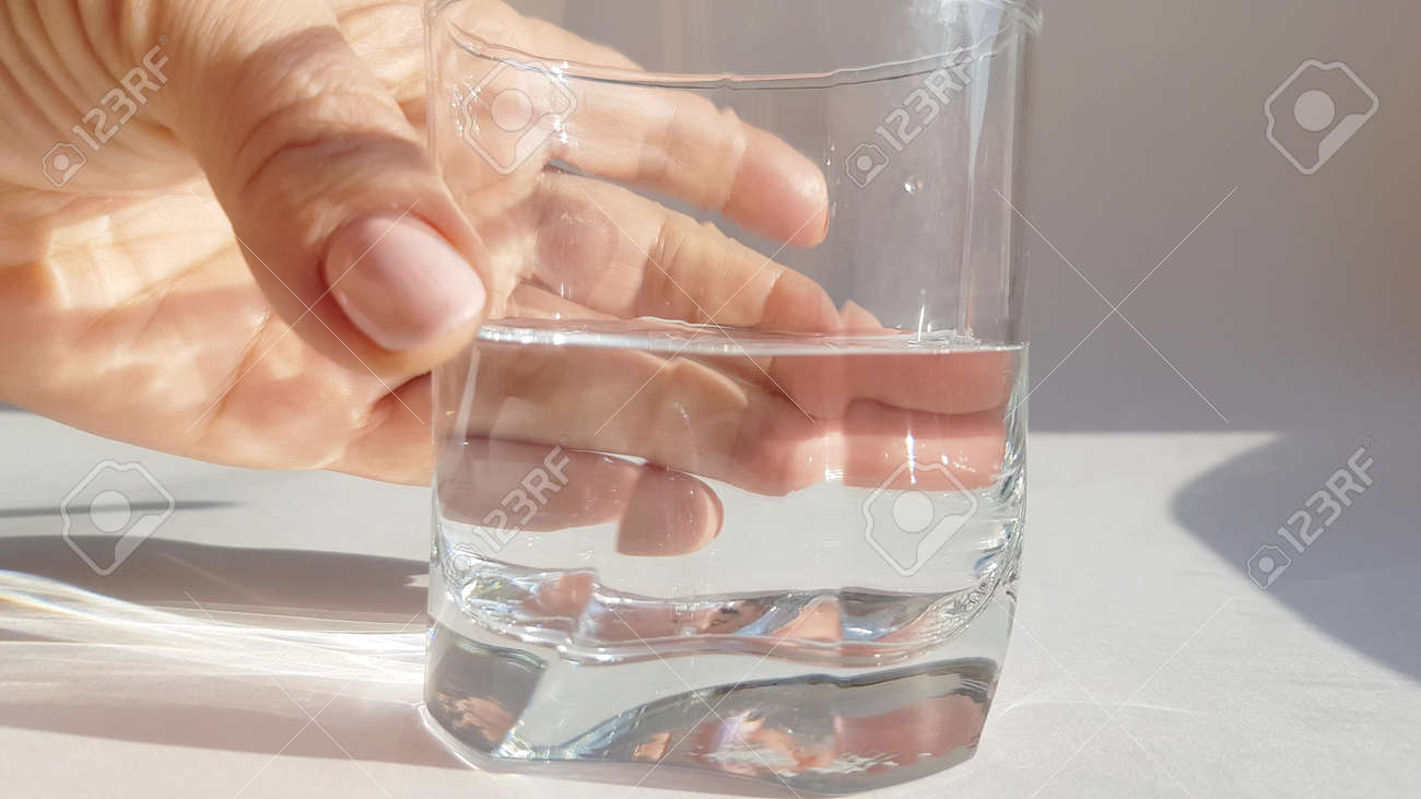 Close-up of female hand holding transparent glass with cold water on white background - 168250778 Close-up of female hand holding transparent glass with cold water on white background - 168250778